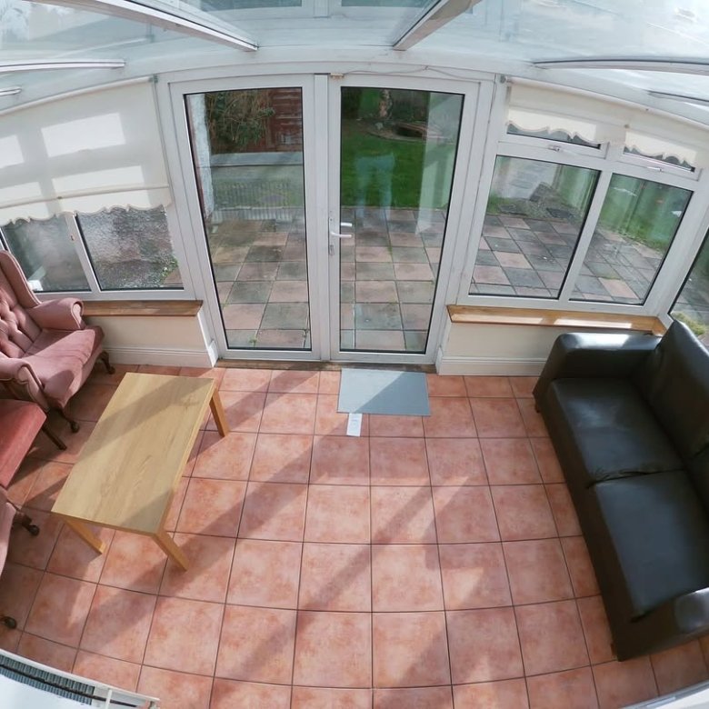 Sunroom interior with pink armchairs, leather sofa, and tiled floor.