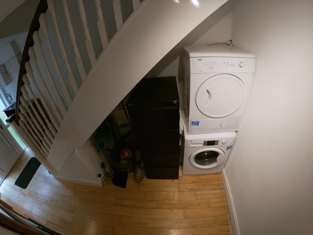 Stacked washer and dryer under stairs with black storage unit.