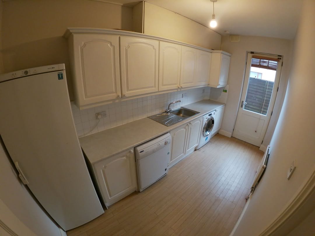 White kitchen with cabinets, appliances, and door to the outside.