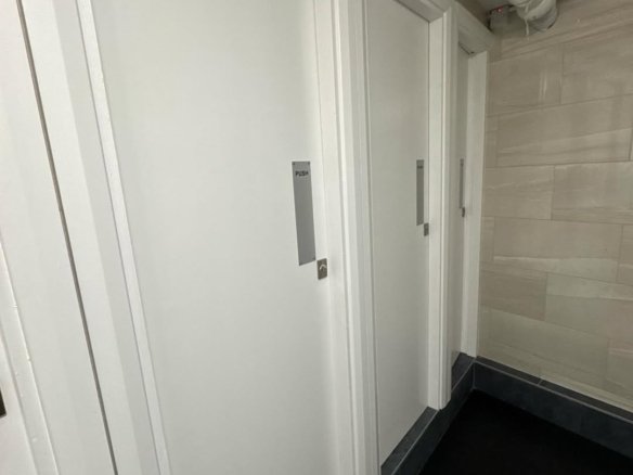 Row of white restroom stall doors with push plates in a public space.