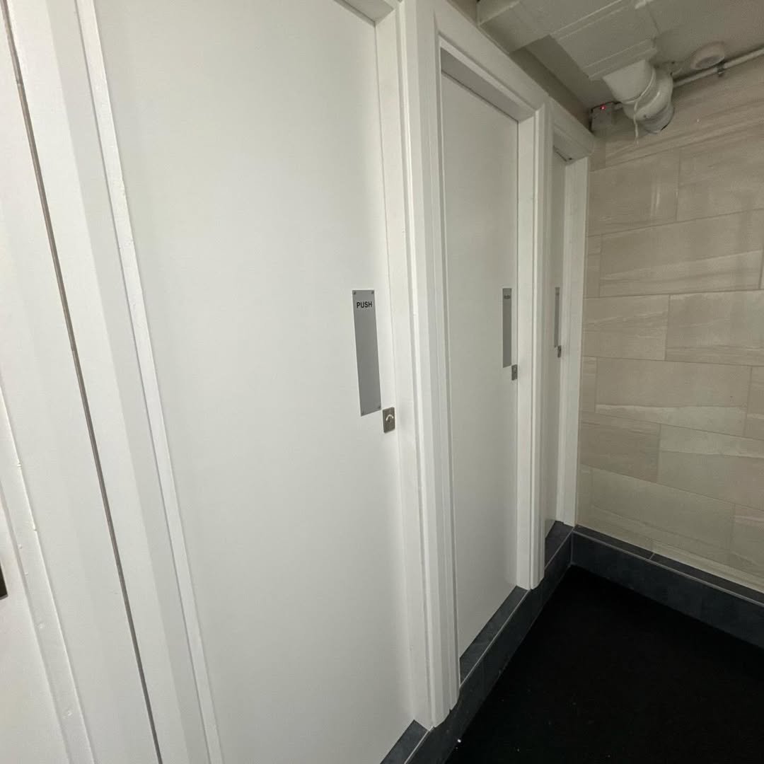 Row of white restroom stall doors with push plates in a public space.