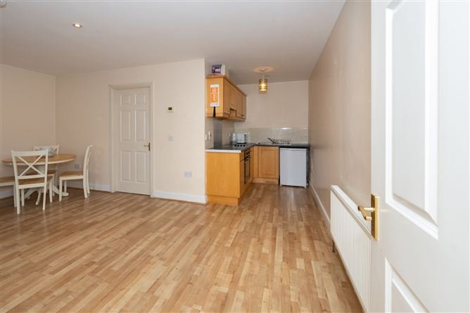 Apartment interior with wood floors, dining table, kitchenette, and white door.