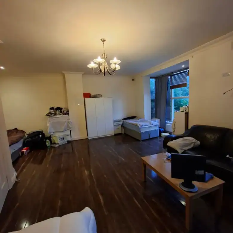 Spacious apartment interior with dark wood floors, bed, sofa, and chandelier lighting.