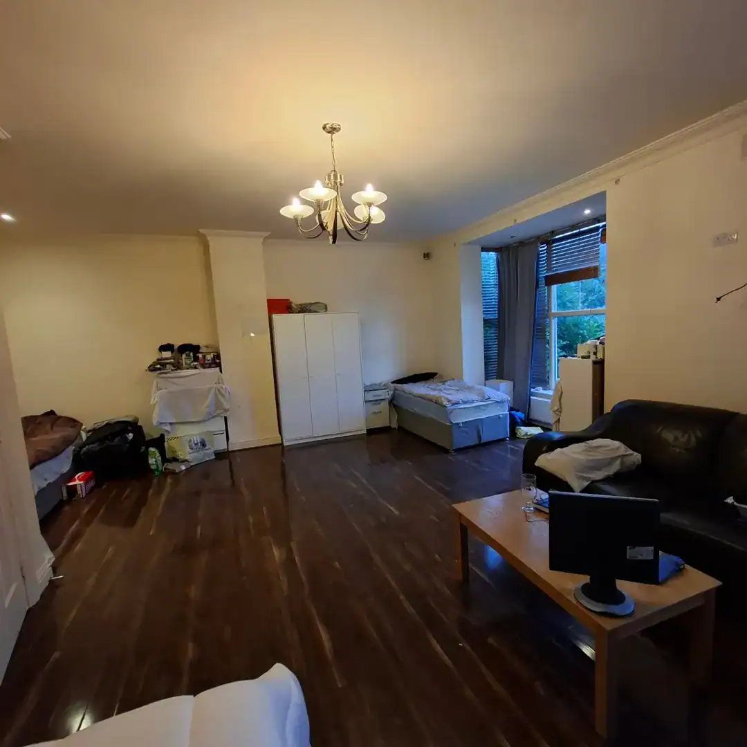 Spacious apartment interior with dark wood floors, bed, sofa, and chandelier lighting.