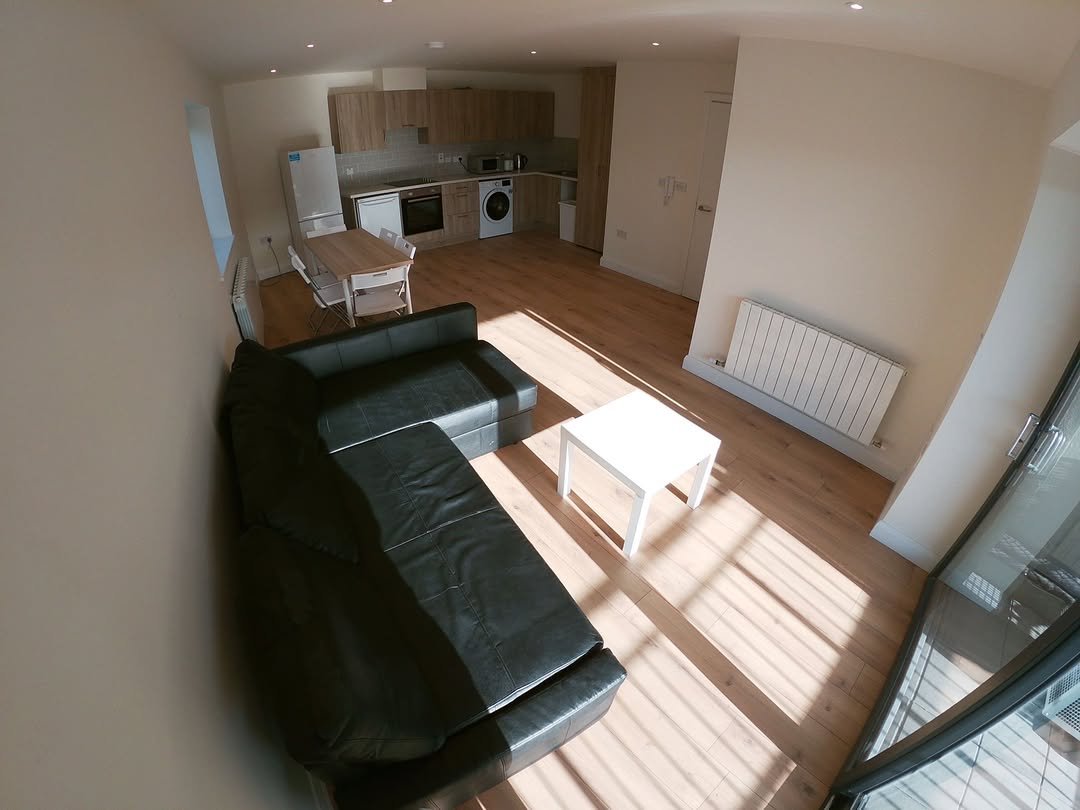 Apartment living room: black sofa, white table, open kitchen, hardwood floors.