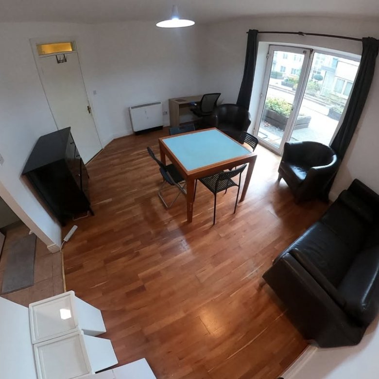 Apartment living room with furniture, including a table, chairs, and a black leather sofa.
