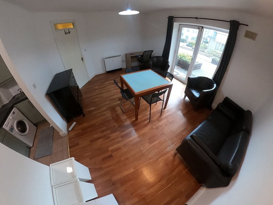 Apartment living room with furniture, including a table, chairs, and a black leather sofa.