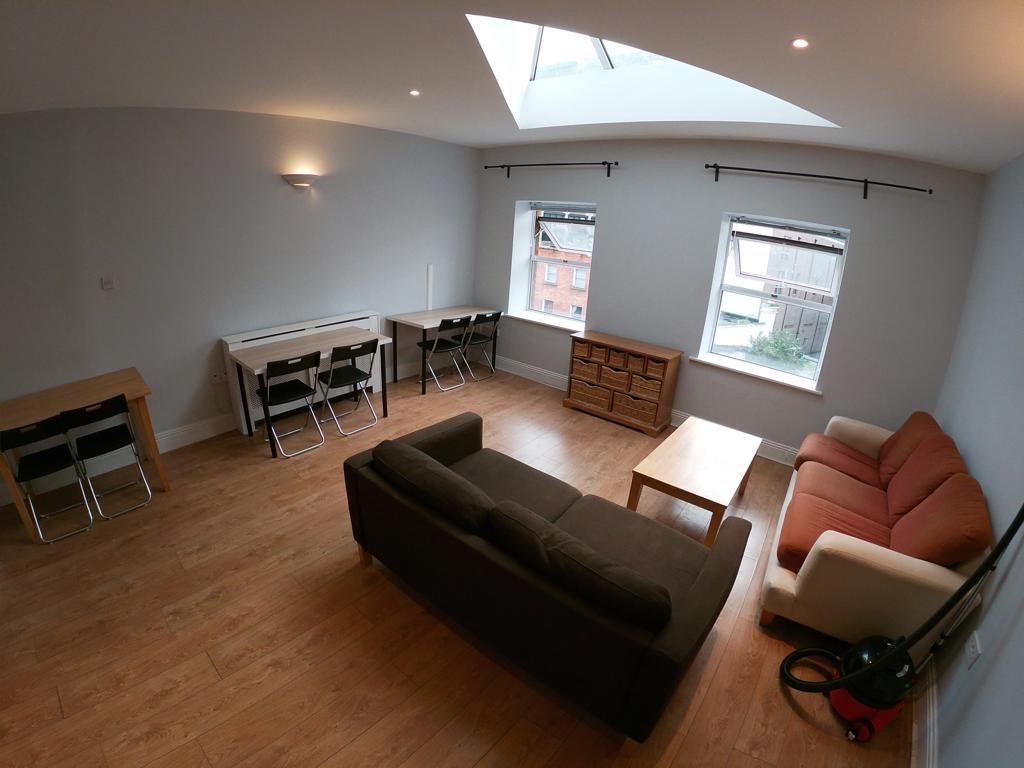 Bright apartment living room with sofas, desks, and natural light from skylight and windows.