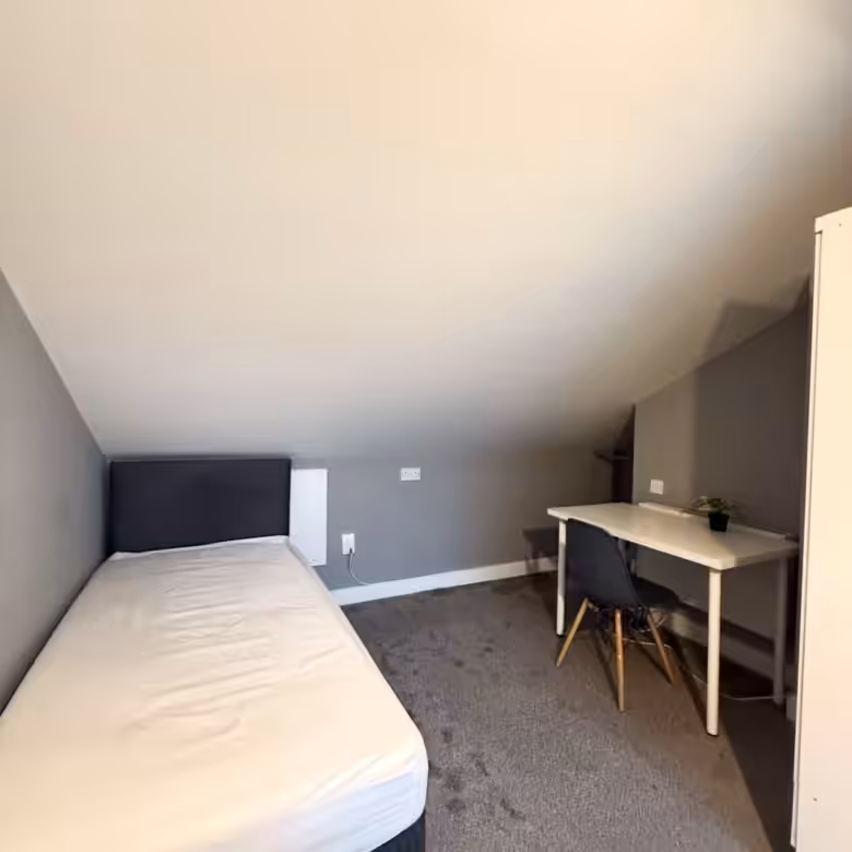 Attic bedroom with bed, desk, and chair under a sloping ceiling.