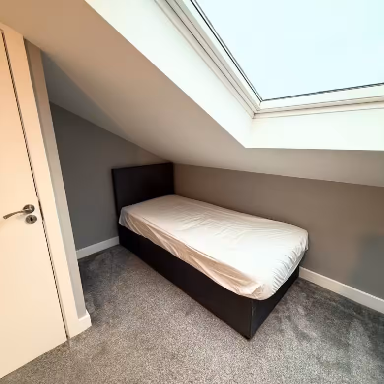 Cozy attic bedroom with single bed under a skylight window.