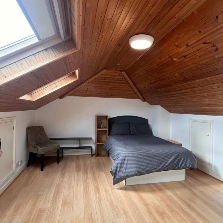 Attic bedroom with skylight, wooden ceiling, and grey bedding.
