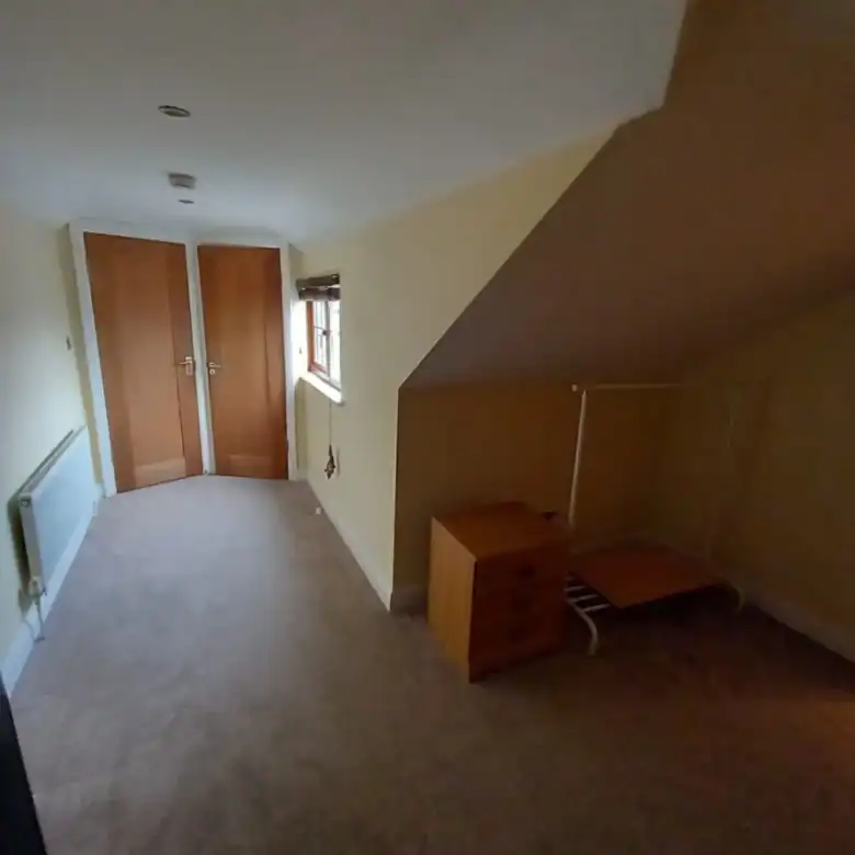 Attic bedroom with sloped ceiling, wardrobe, dresser, and clothes rack.