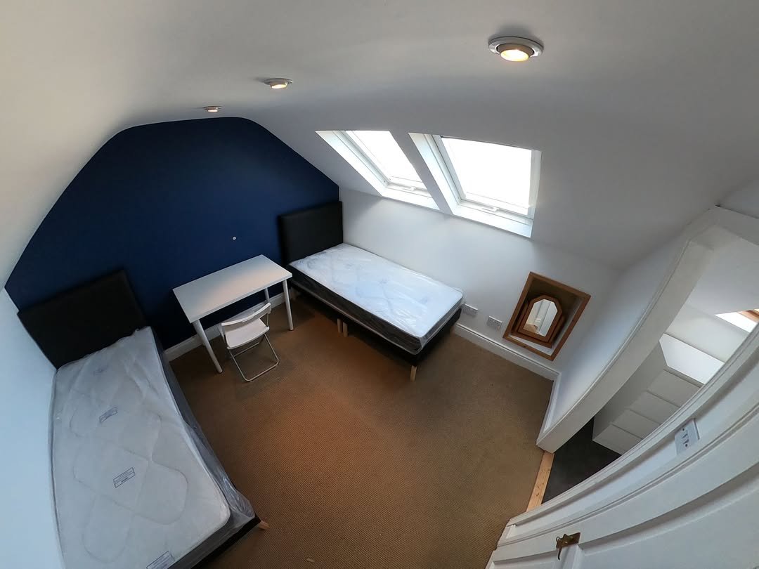 Attic bedroom with two beds, desk, and skylight. Blue accent wall.