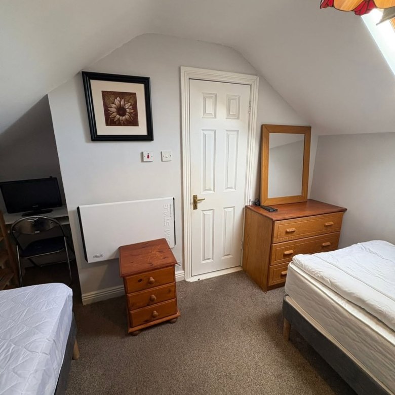 Cozy bedroom with two beds, dresser, and desk in an attic room.