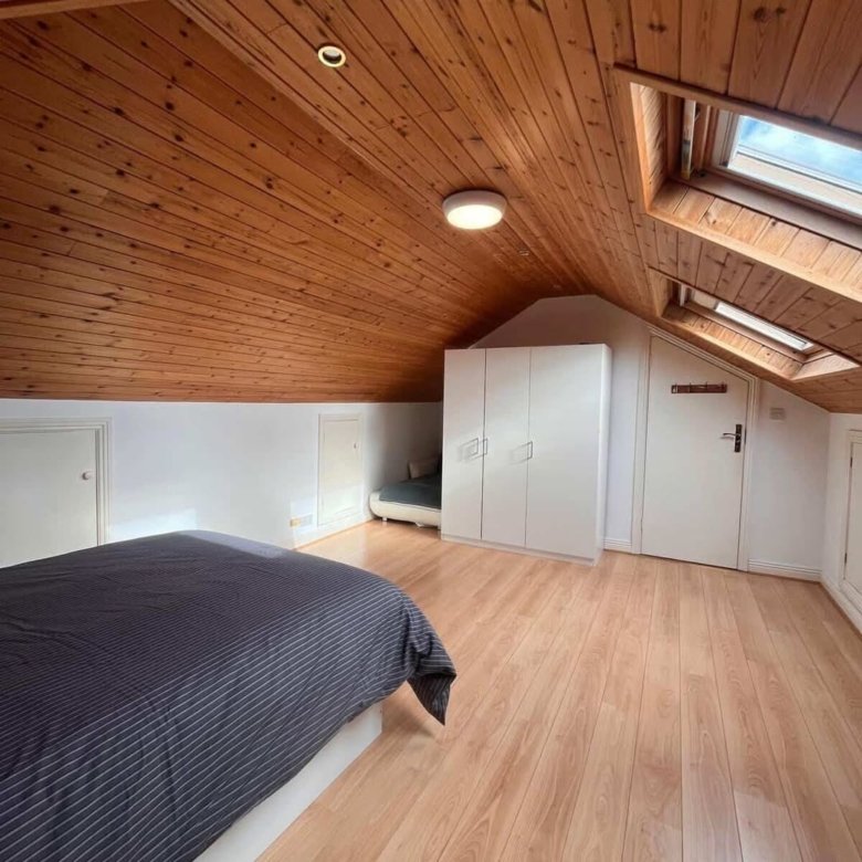 Attic bedroom with wooden ceiling, skylights, bed, and white wardrobe.