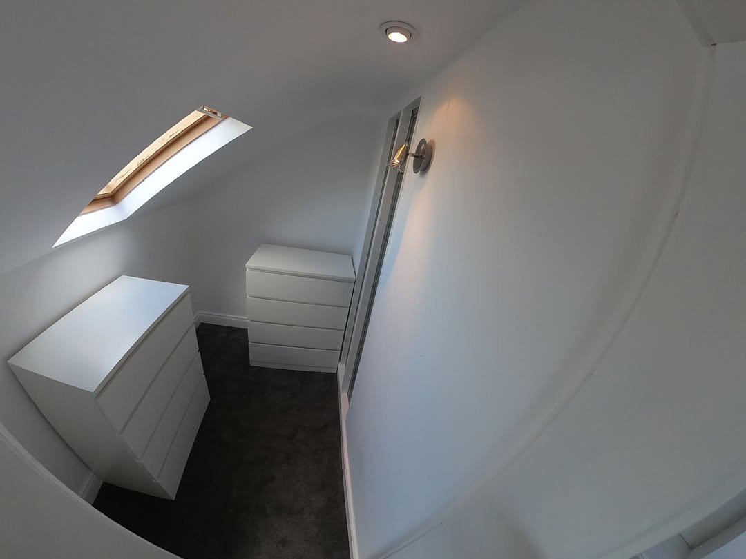 Attic room with skylight, fitted white drawers, and sloped ceiling.