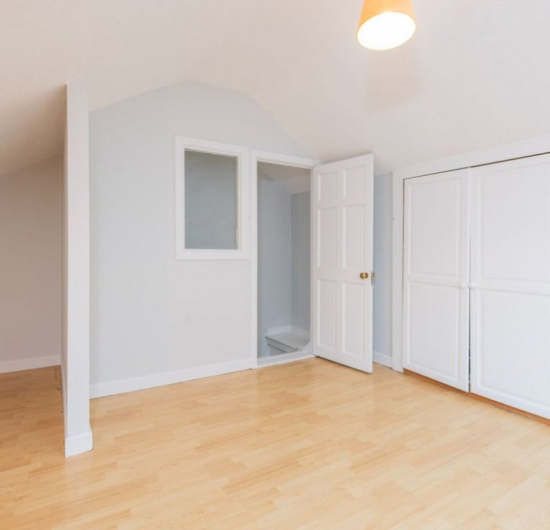 Bright attic room with wood floor, white walls, closet and small window.