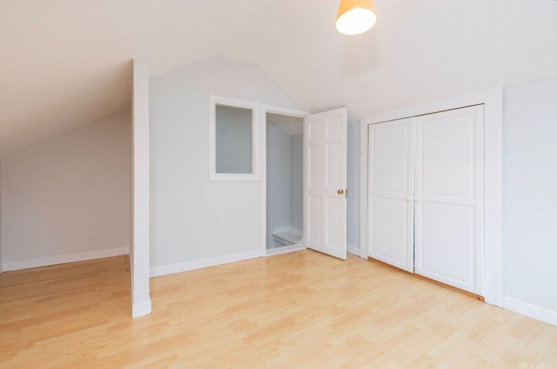 Bright attic room with wood floor, white walls, closet and small window.