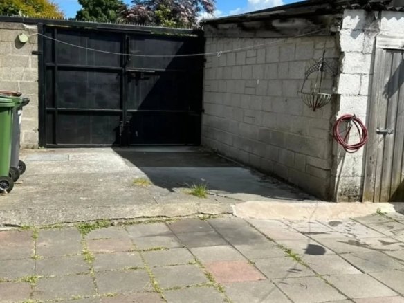 Backyard concrete patio with black metal gate, block wall, and wooden door on a sunny day.