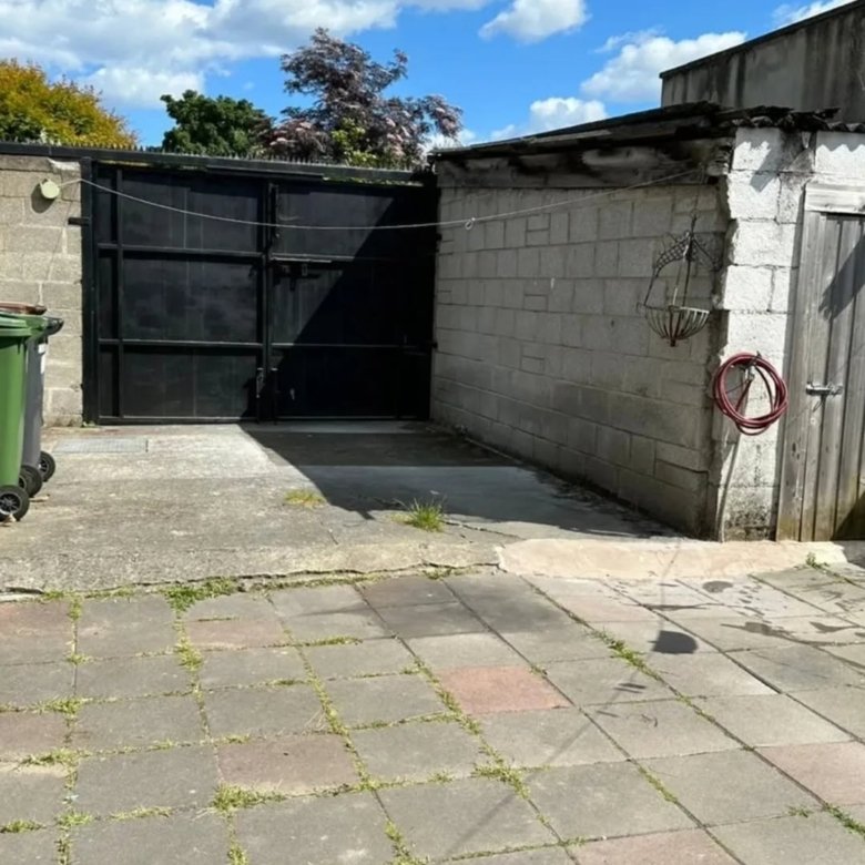 Backyard concrete patio with black metal gate, block wall, and wooden door on a sunny day.