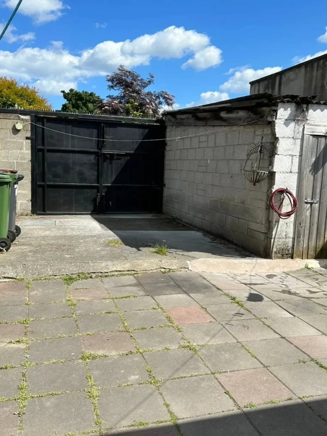 Backyard concrete patio with black metal gate, block wall, and wooden door on a sunny day.