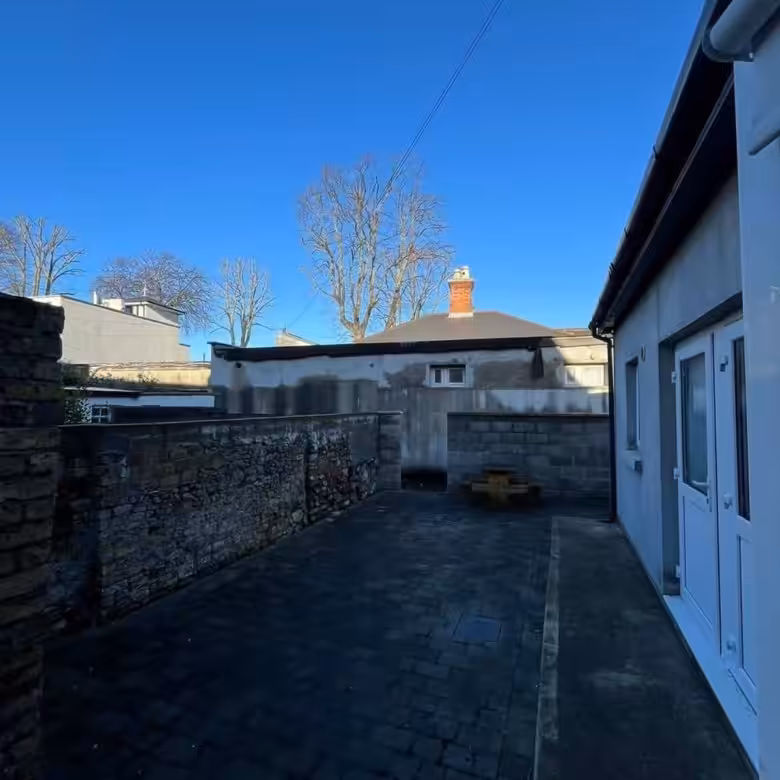 Backyard patio with stone wall, brick paving, and building in the background.