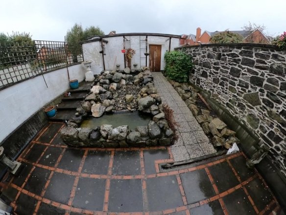 Small backyard pond with rockery and stone-paved patio area.