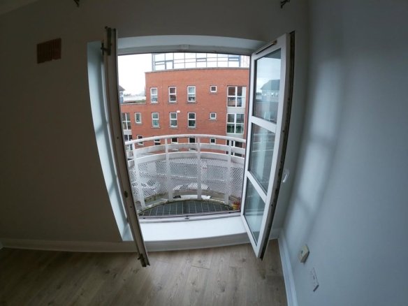 Open balcony doors with view of brick building and white railing.