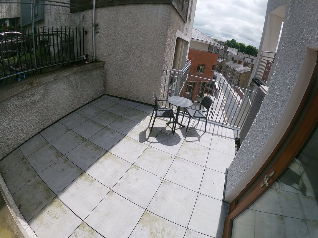 Small balcony with tiled floor, table, and two chairs, overcast day.