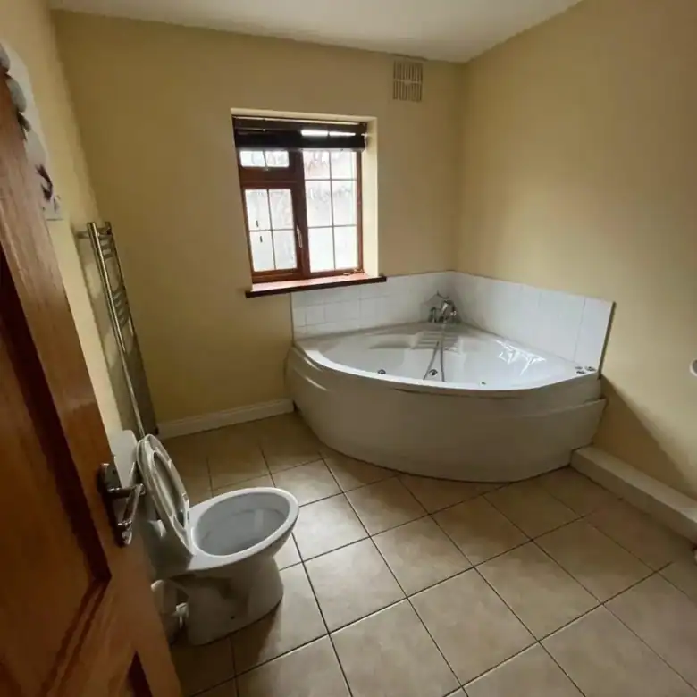 Bathroom with corner jacuzzi tub, toilet, heated towel rack, and small window.
