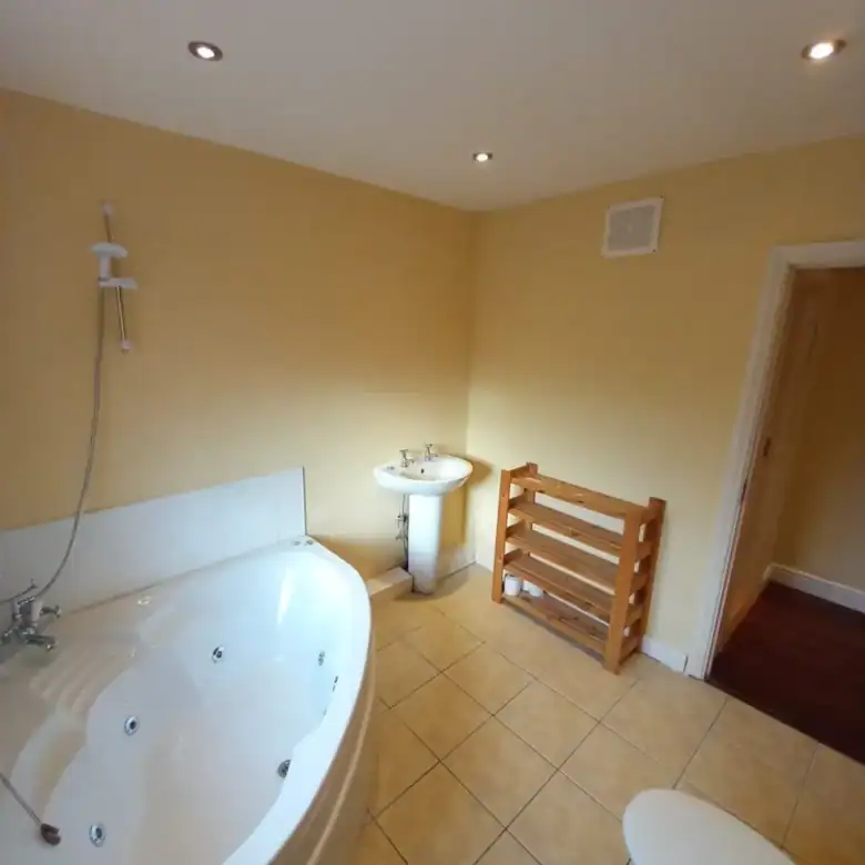 Bathroom interior with jacuzzi tub, pedestal sink, and wooden shelf.