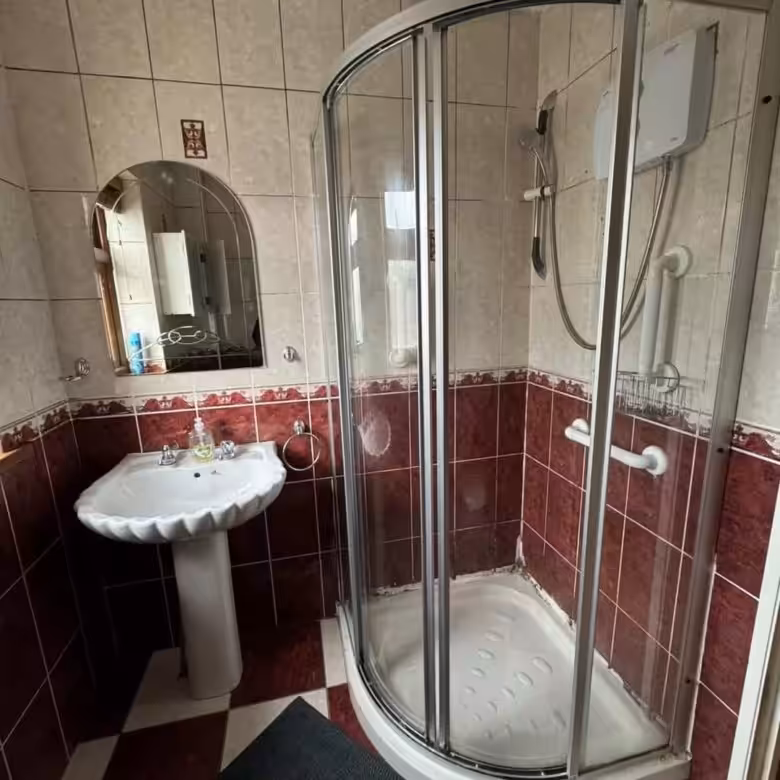 Bathroom with pedestal sink, shower stall, and red/beige tile.