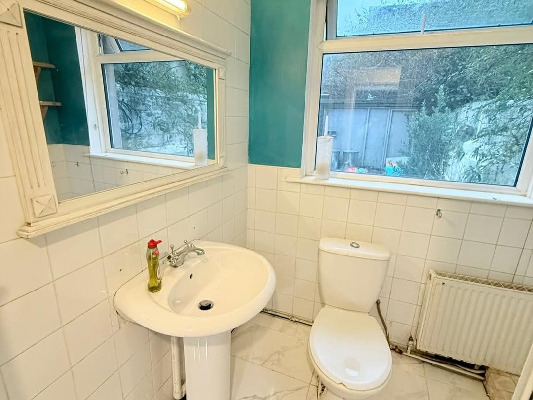 Bathroom with white sink, toilet, and radiator under window.