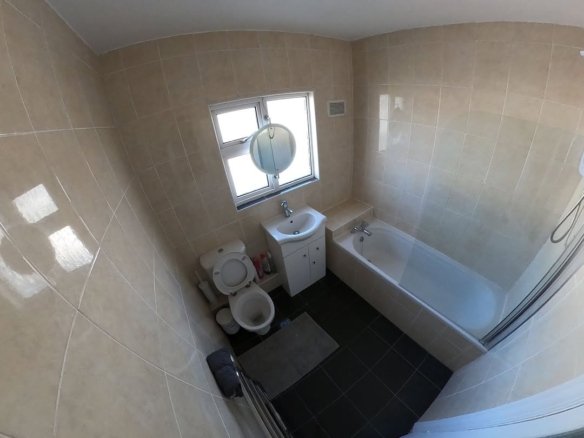 Bathroom with toilet, sink, tub, and window. Beige tile walls and black tile floor.