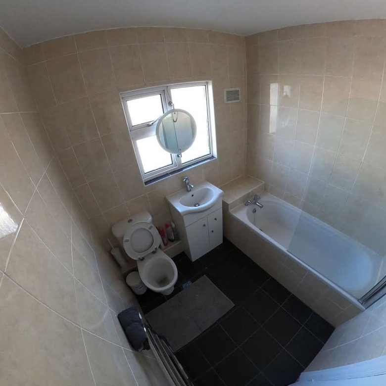 Bathroom with toilet, sink, tub, and window. Beige tile walls and black tile floor.