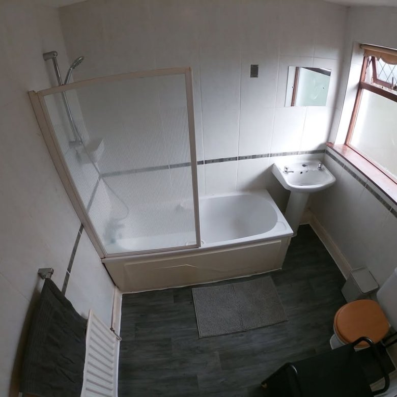 Bathroom with tub, shower, sink, toilet, and gray flooring. Window provides natural light.