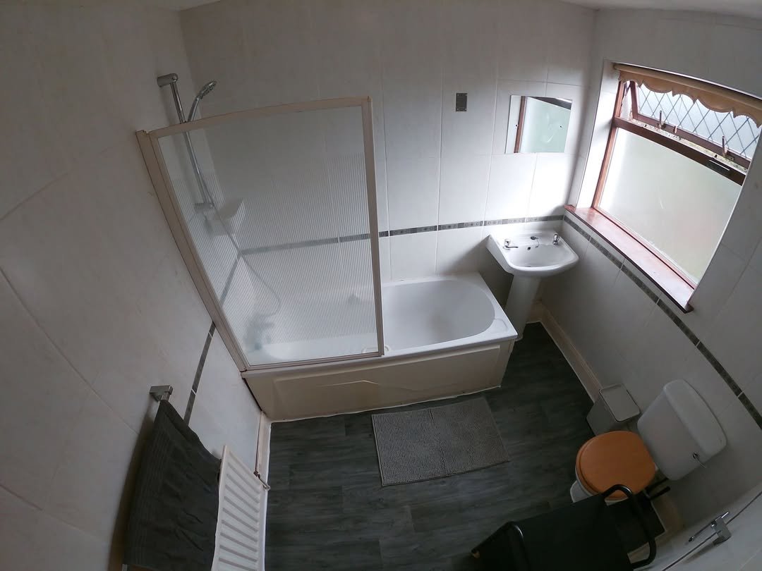 Bathroom with tub, shower, sink, toilet, and gray flooring. Window provides natural light.