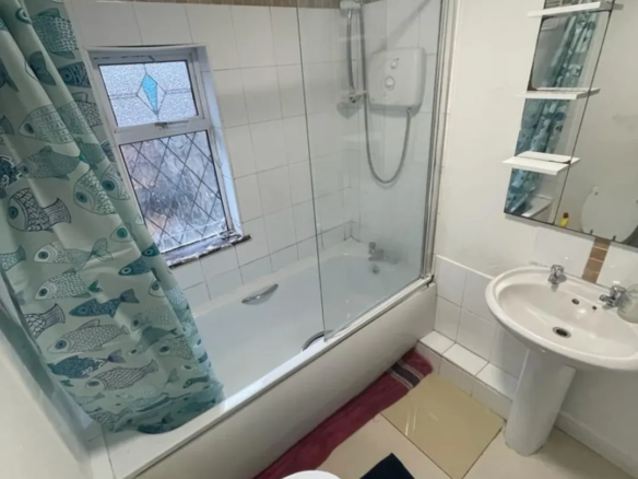 Bathroom with tub, shower, toilet, sink, and fish-themed shower curtain.