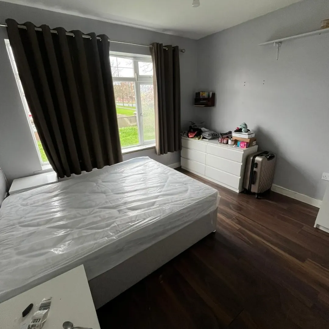 Bedroom with a bed, dresser, suitcase, and dark curtains in front of a window.