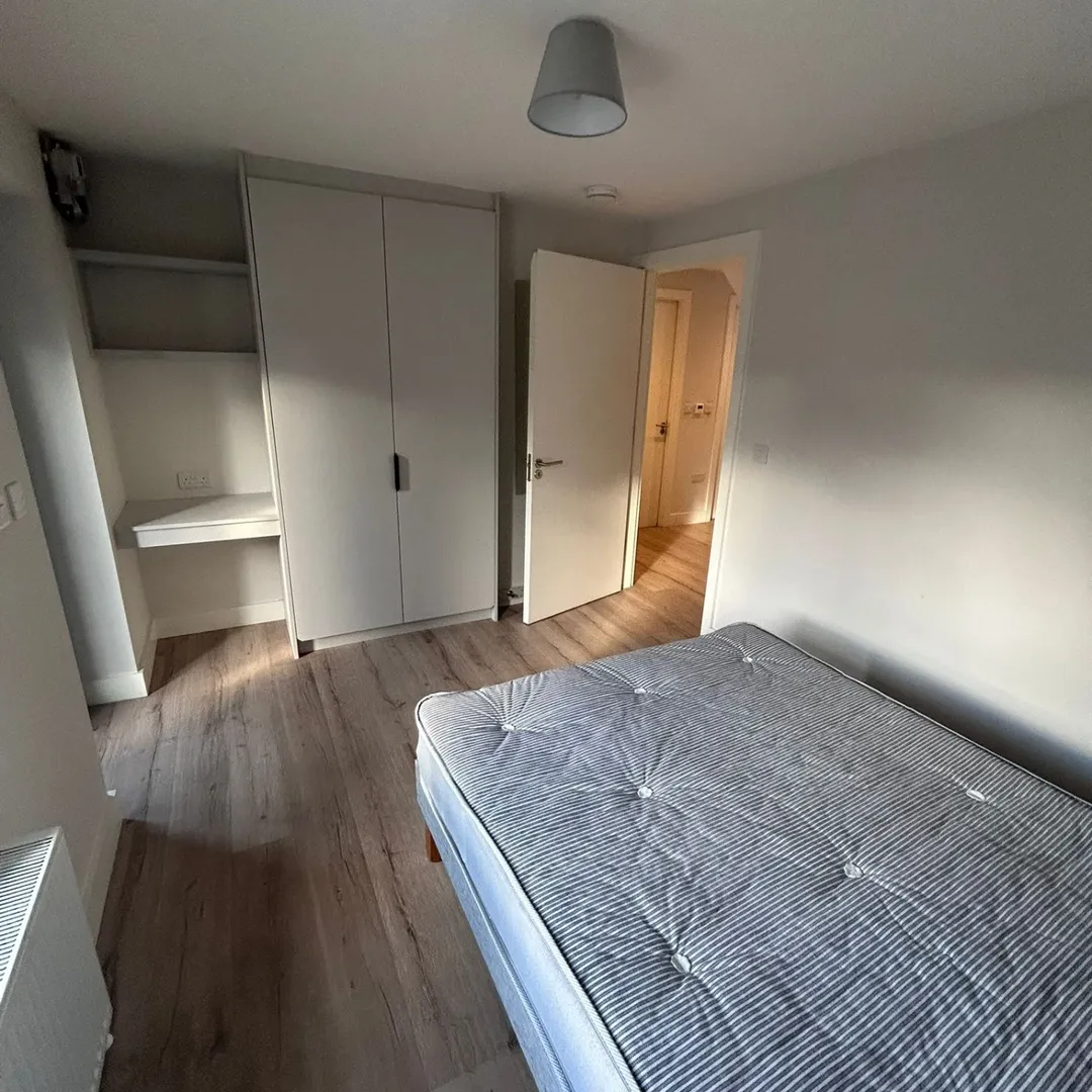 Cozy bedroom with bed, wardrobe, and desk. Neutral tones, wood floor.