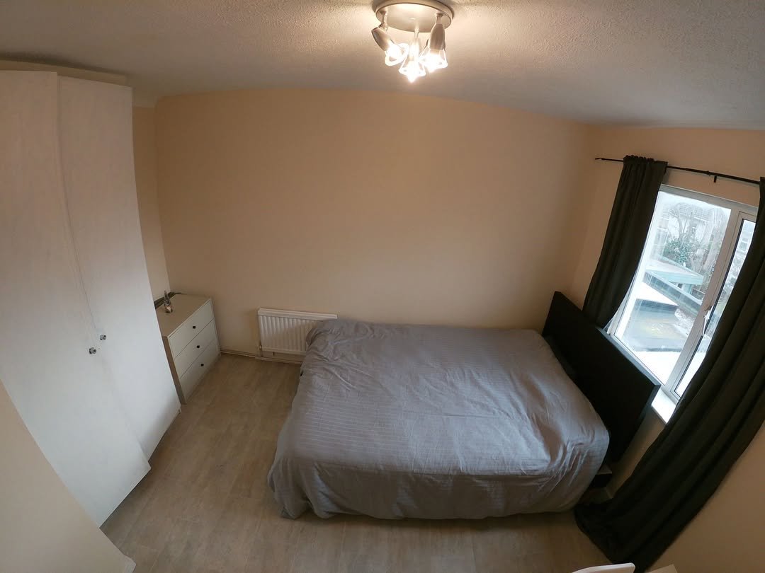 Bedroom with bed, wardrobe, dresser, and window with curtains.