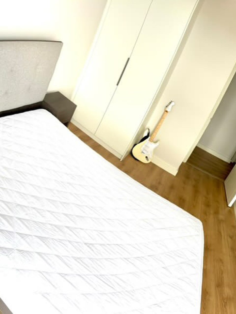 Bedroom with bed, wardrobe, and guitar. Minimalist interior design.