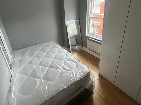 Bedroom with bed, wardrobe, mirror, and window. Gray walls and wood floor.