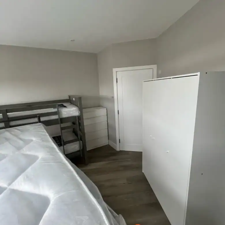 Bedroom with bunk bed, dresser, and white wardrobe. Neutral decor.