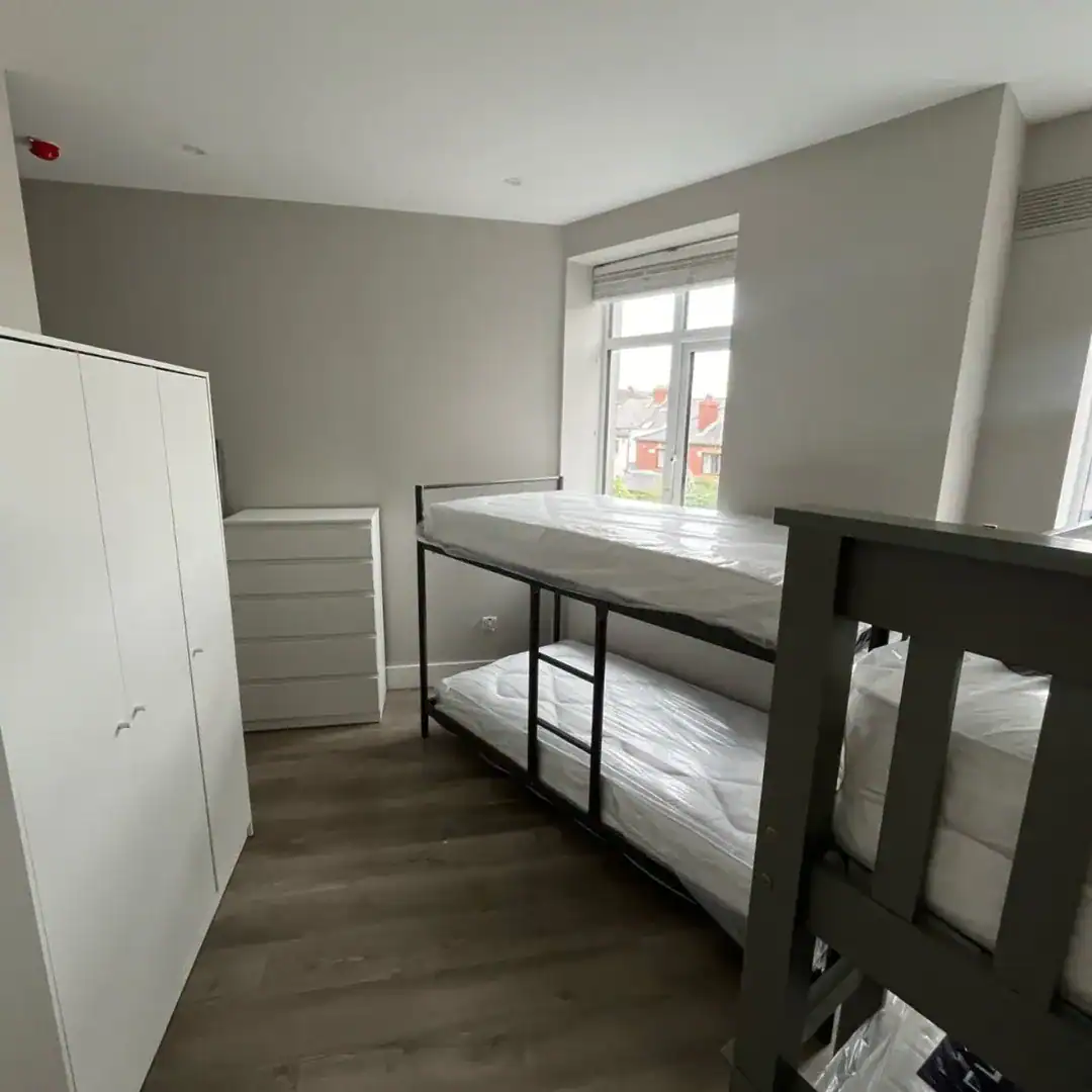 Bedroom with bunk bed, white wardrobe, and chest of drawers. Neutral tones.