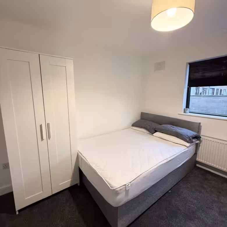 Bedroom with double bed, wardrobe, window, and dark carpet.