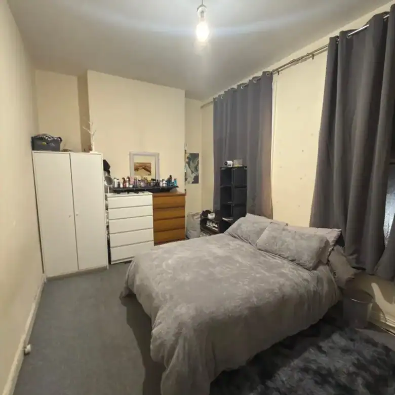 Bedroom interior with bed, dresser, wardrobe, and dark gray curtains.