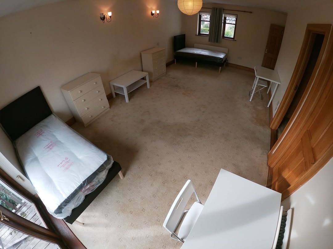 Bedroom with single bed, desk, and storage. Neutral carpet and light walls.
