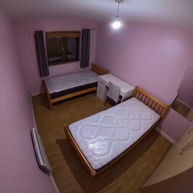 Bedroom with two single beds, desk, wardrobe, window, and pink walls.