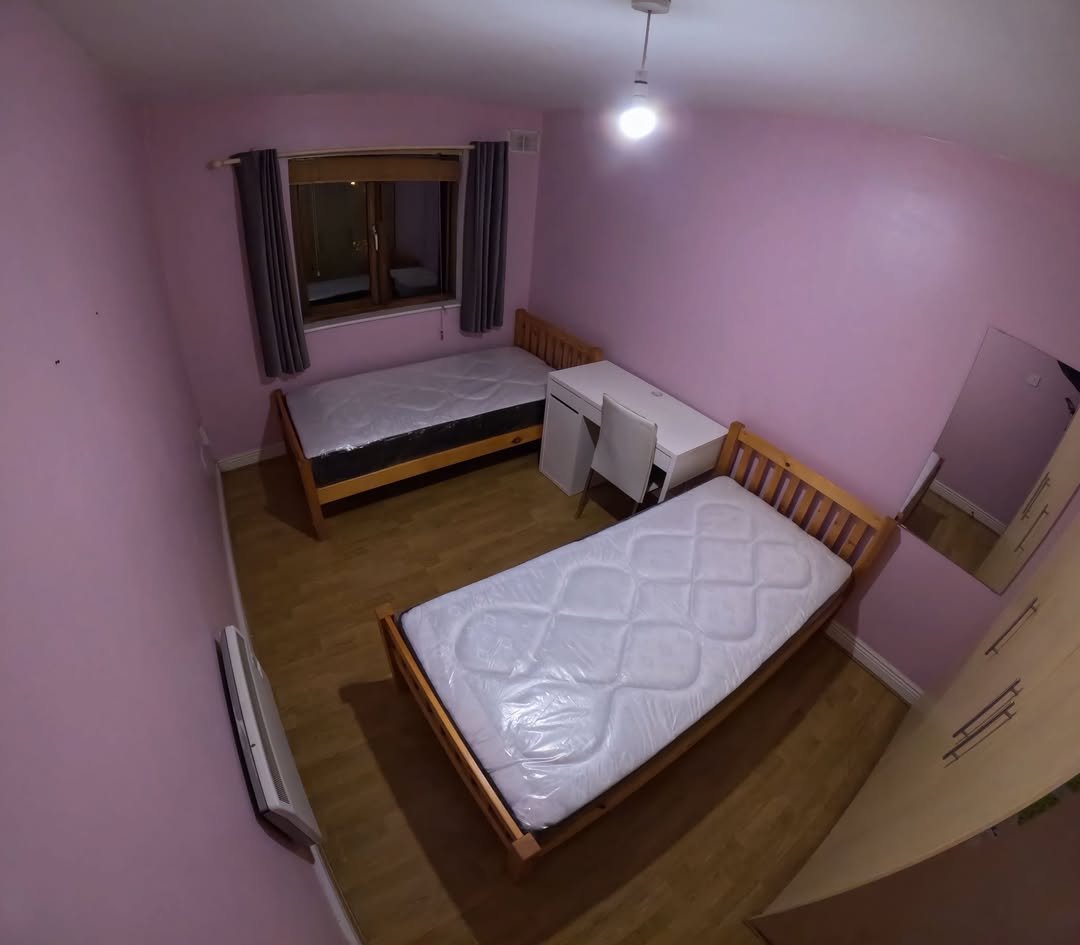 Bedroom with two single beds, desk, wardrobe, window, and pink walls.